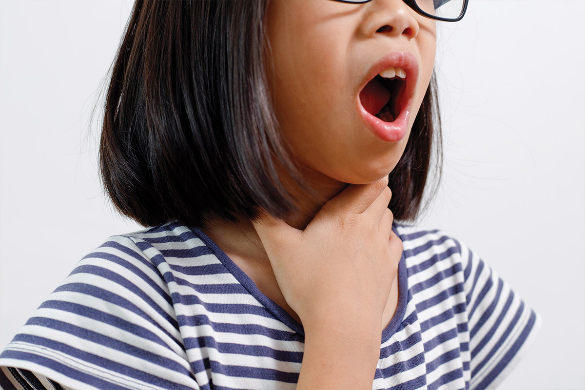 A young girl with glasses appears to be yawning and holding her throat, wearing a striped shirt against a light background.