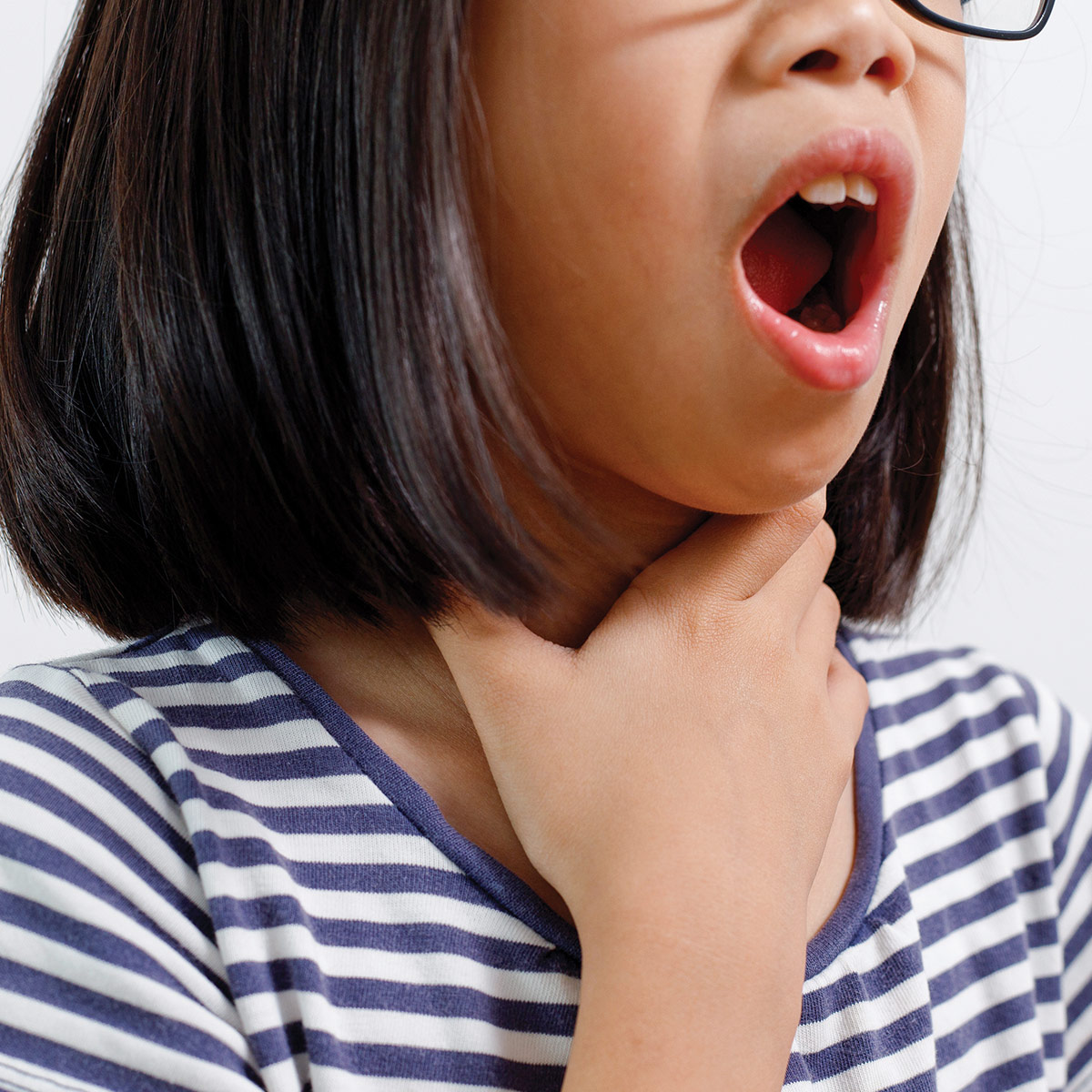 A young girl with glasses appears to be yawning and holding her throat, wearing a striped shirt against a light background.