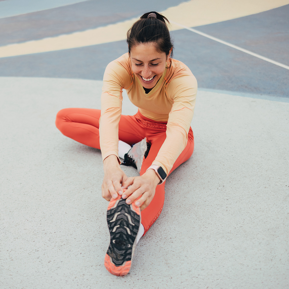 A woman in activewear stretches her leg while sitting on a colorful track, smiling and enjoying her workout.