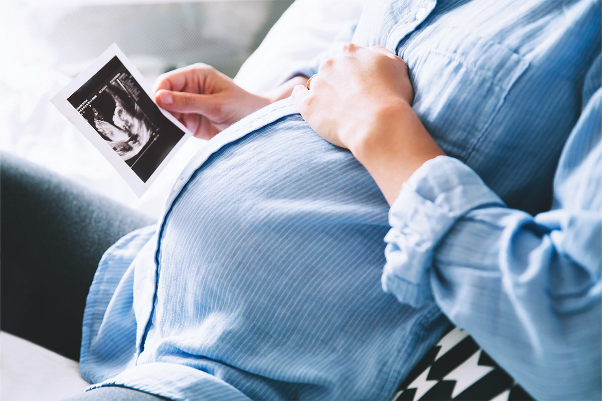 pregnant woman with her hand on her belly holding an ultrasound photo