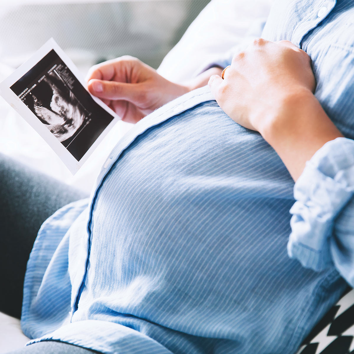 pregnant woman with her hand on her belly holding an ultrasound photo