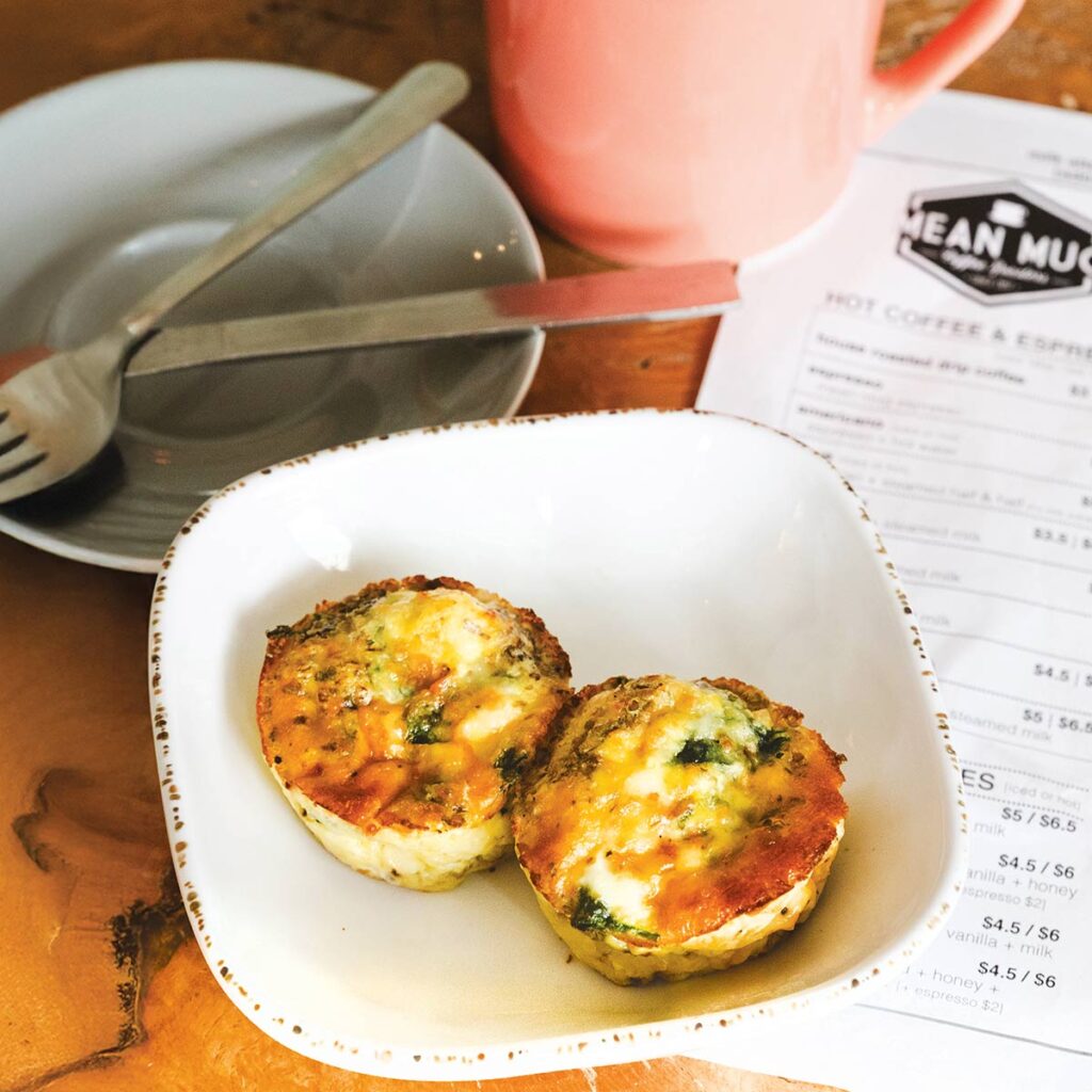 Two savory baked egg muffins topped with herbs, served in a small white dish on a wooden table beside a menu.