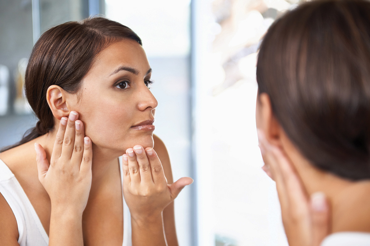woman looking at skin in mirror