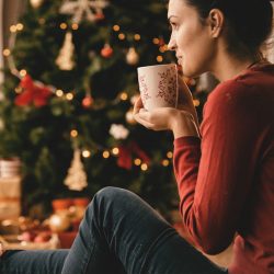 woman sitting by a christmas tree with a coffee