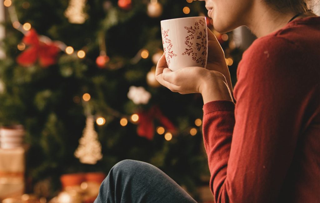 woman sitting by a christmas tree with a coffee